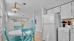 A modern kitchen with white cabinets, a large refrigerator, and teal chairs around a white table.