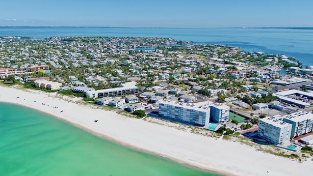 An aerial view of a coastal resort area with beachfront properties, a large hotel complex, and a bridge in the distance.