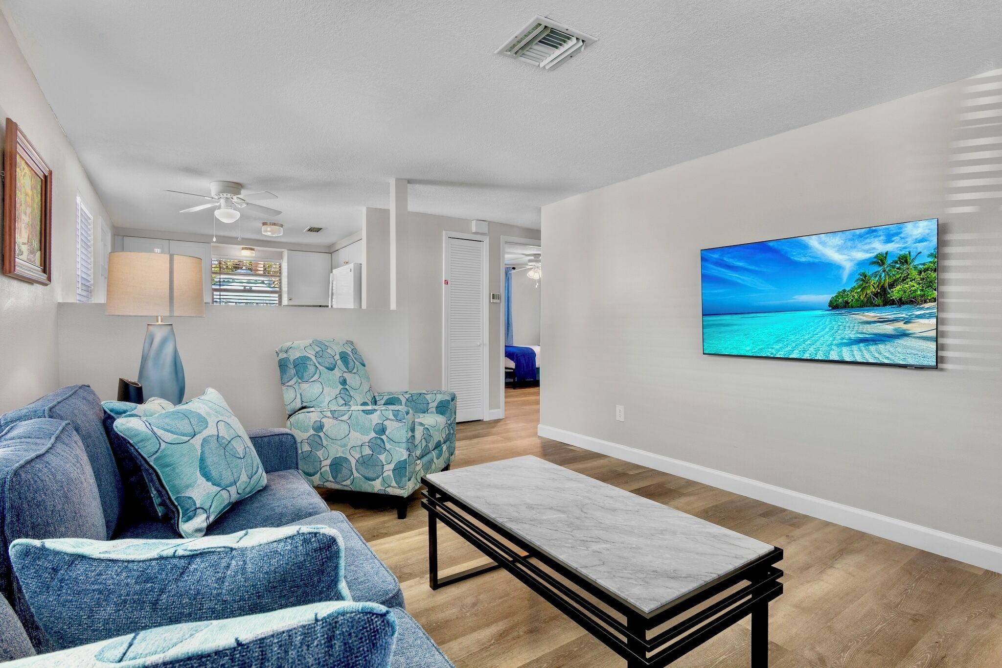 A living room with a sofa, armchair, and a coffee table. There is a painting of a beach on the wall.