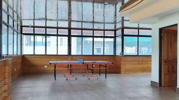 Una habitación amplia con mesa de ping pong, ventanas grandes y pisos de madera.