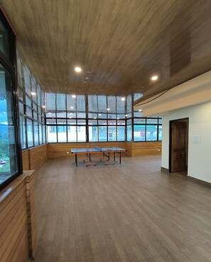 A spacious room with wooden floors, large windows, and a ping pong table.