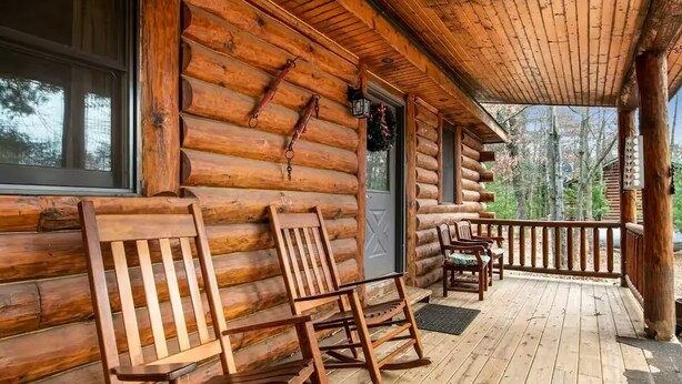 A log cabin with a porch featuring rocking chairs and a table.