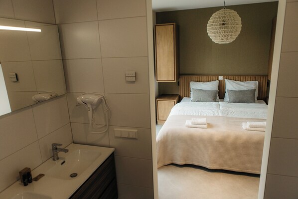 Una habitación de hotel moderna con una cama grande, un baño con lavamanos y un secador de pelo, y una lámpara colgante.