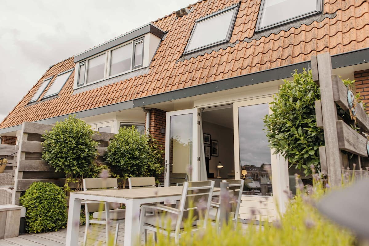 A residential building with a sloped roof, large windows, and a patio area with a table and chairs.