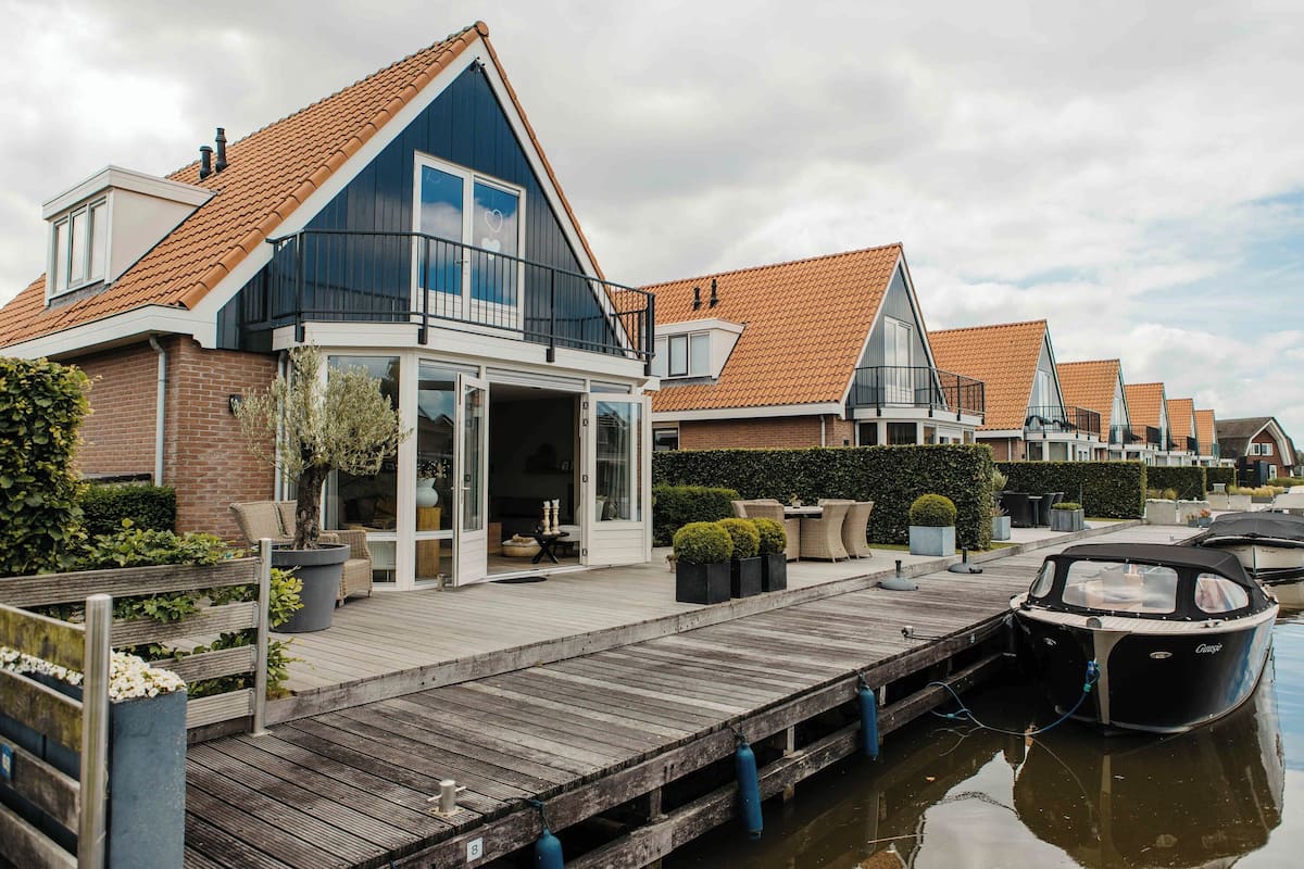 A row of modern houses with a wooden dock extending into a calm water body, connected by a bridge.