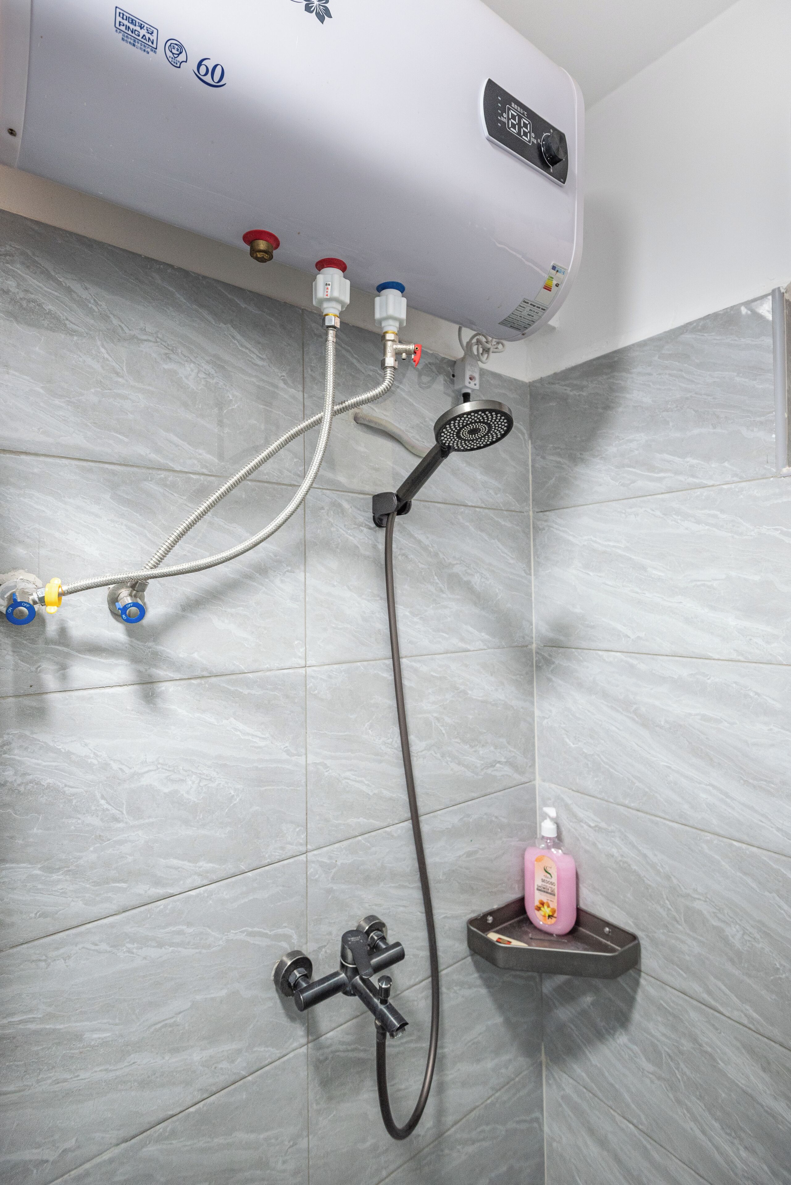 A bathroom with a built-in shower, a water heater, and a soap dispenser on a shelf.