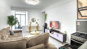 A modern living room with a sofa, coffee table, TV, and a kitchen area with a stove.