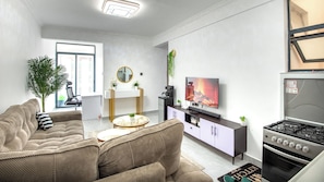A modern living room with a sofa, coffee table, TV, and a kitchen area with a stove.