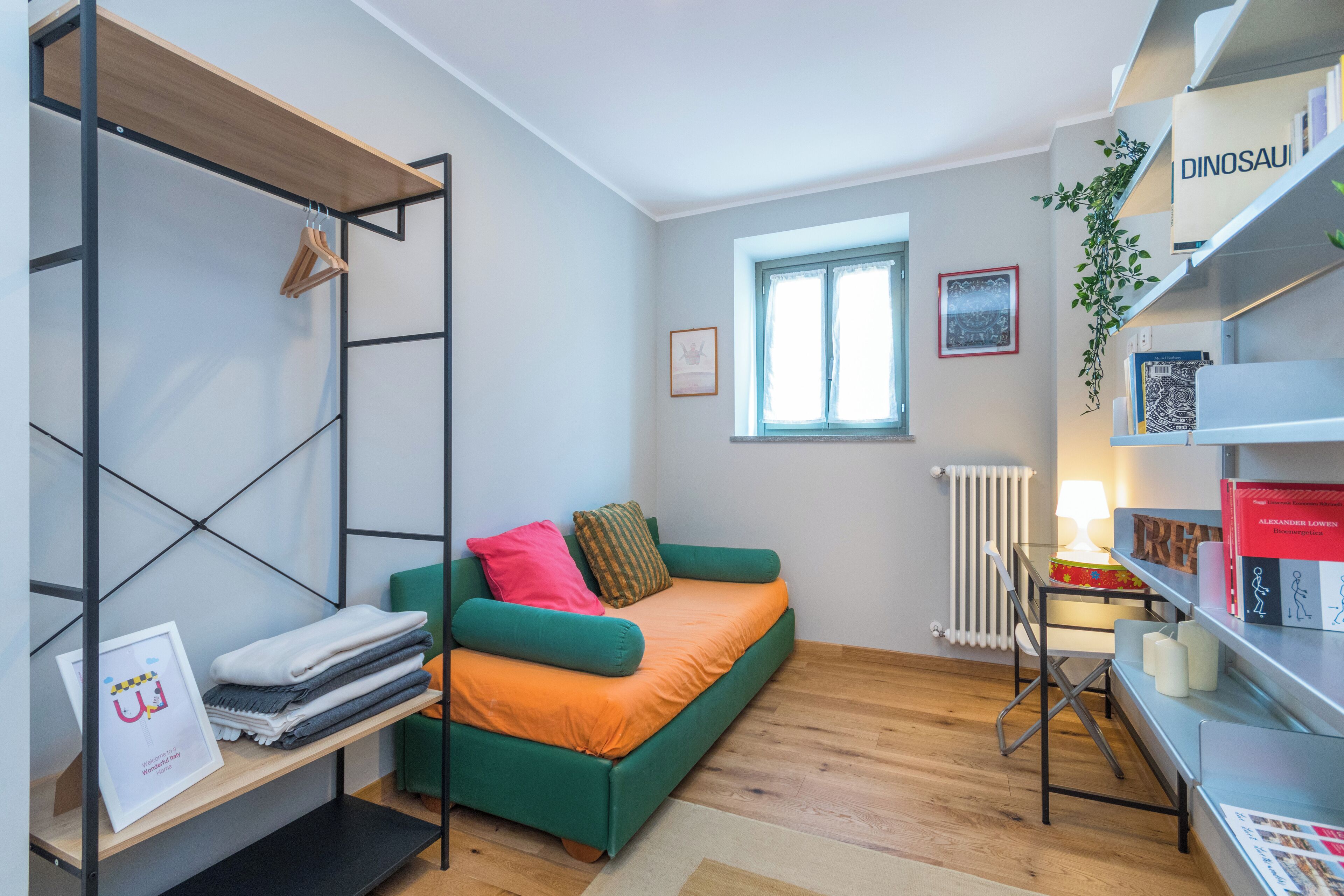 Una camera compatta con un letto a castello, un divano letto, un termosifone, una finestra e una libreria.