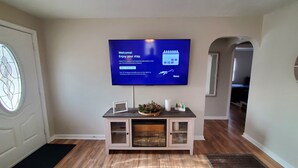 A room with a flat-screen TV mounted on the wall, a small wooden console table with a decorative bowl, and a door with a stained glass window. - Cozy 2-bedroom house in Marion that is perfect for a relaxing stay (Marion)