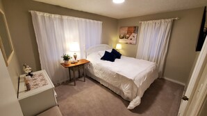 A bedroom with a bed, a bedside table with a lamp, a small desk with a plant, and a picture on the wall. - Cozy 2-bedroom house in Marion that is perfect for a relaxing stay (Marion)