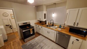 A compact kitchen with white cabinets, a stainless steel oven, a dishwasher, and a wooden countertop. - Cozy 2-bedroom house in Marion that is perfect for a relaxing stay (Marion)