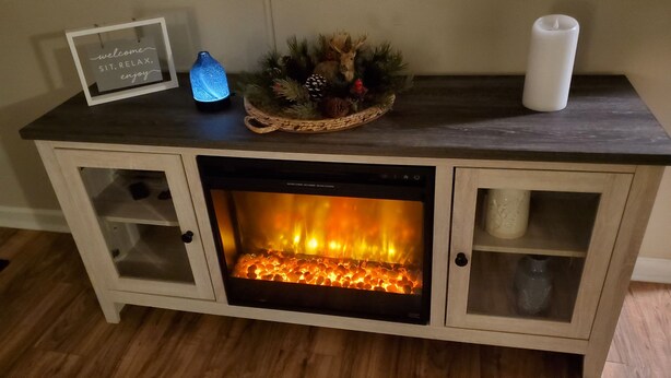 A fireplace with a glass door, a framed welcome sign, a blue glass bottle, and a candle on the mantel. - Cozy 2-bedroom house in Marion that is perfect for a relaxing stay (Marion)