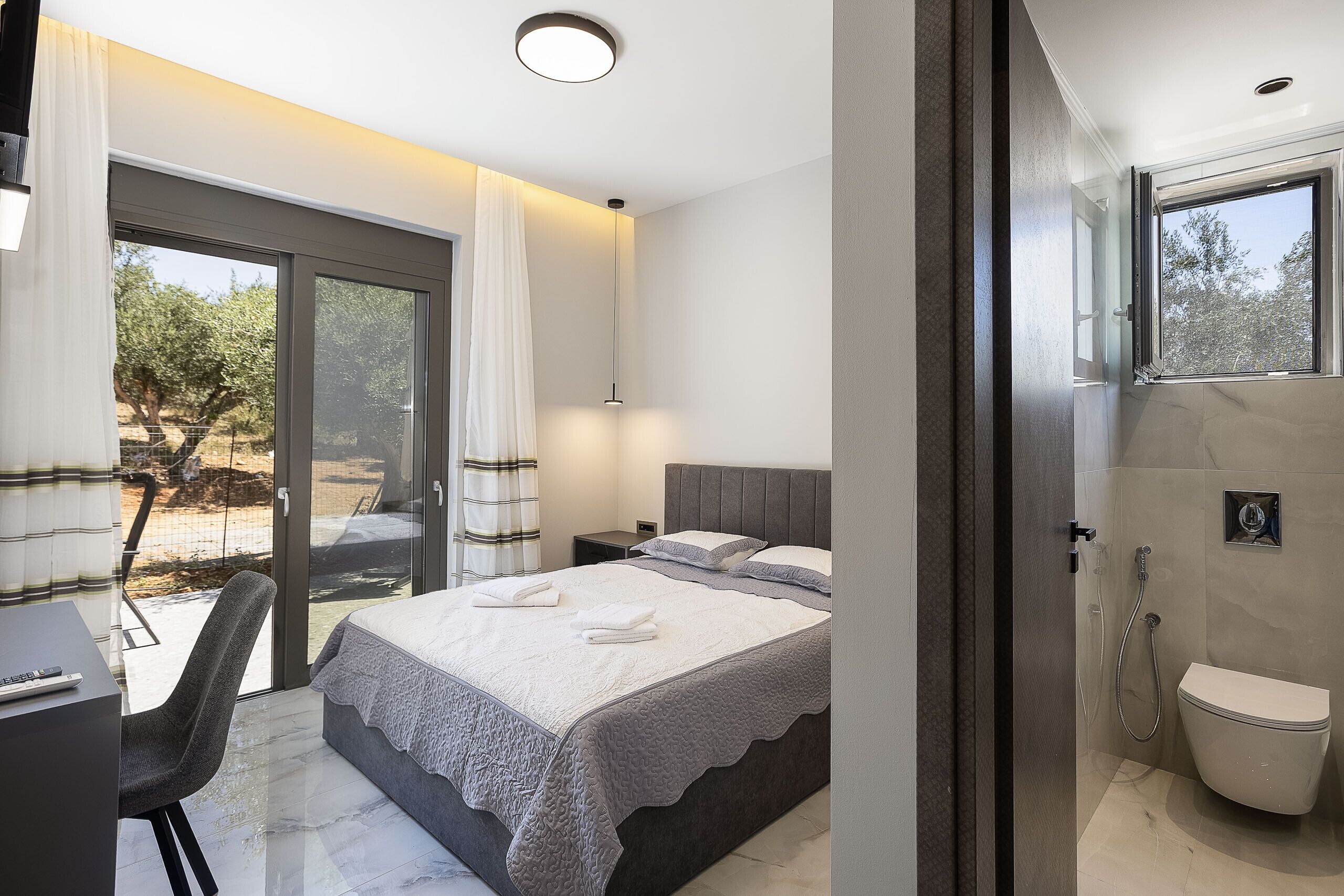 A modern bedroom with a bed, bedside tables, a desk, and a shower area.