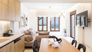 A modern kitchen with a wooden countertop, a dining table with chairs, a sofa, and a TV mounted on the wall. - Santa Irini Villas - With 3 Heated Pools (Rethymno)