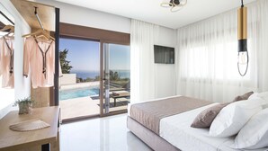 A modern bedroom with a large bed, a wooden side table, a hanging plant, and a view of a swimming pool and ocean. - Santa Irini Villas - With 3 Heated Pools (Rethymno)
