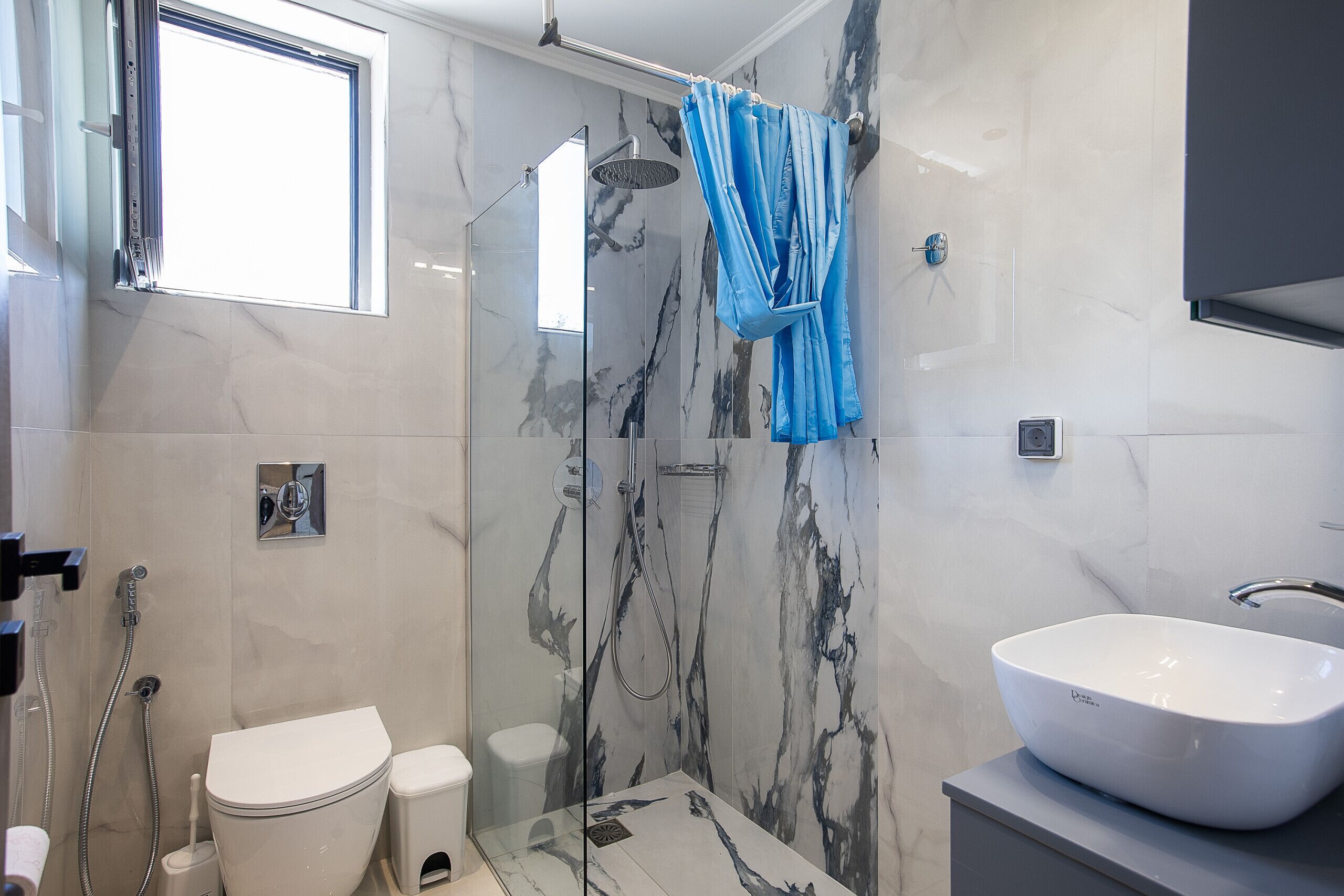 Un baño moderno con ducha de vidrio, lavamanos blanco y retrete.