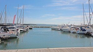 Un port esportiu amb diverses embarcacions amarrades, un moll de fusta i un cel serè.