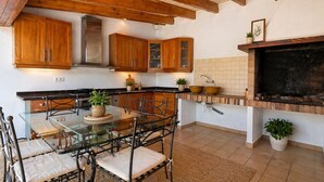 A kitchen with wooden cabinets, a glass dining table, chairs, a brick fireplace, and potted plants.