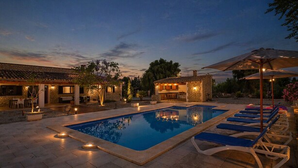 A swimming pool with lounge chairs, a bar area, and outdoor lighting.