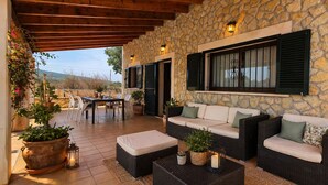 An outdoor patio with wicker furniture, stone walls, and potted plants.