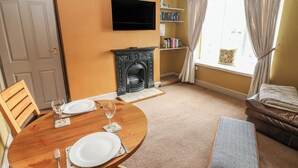 Un coin repas avec une table en bois dressée pour deux personnes, une cheminée, une bibliothèque et un téléviseur fixé au mur.