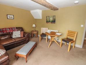 A living room with a brown leather sofa, a wooden dining table with chairs, a bench, and a painting of a forest on the wall. - Ewe Cottage (Ripon)
