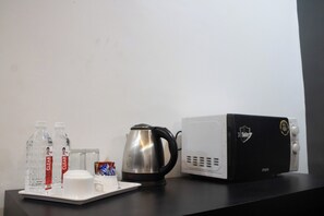 Una kitchenette con cafetera, dos botellas de agua, una taza y un microondas.