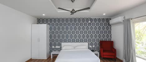 A bedroom with a bed, a red chair, a wardrobe, a ceiling fan, and patterned wallpaper.