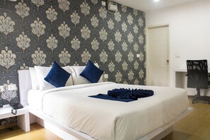 A neatly made bed with white and blue bedding, a bedside table with a phone, and a patterned wallpaper.