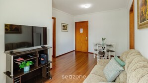 Ein Wohnzimmer mit einem Flachbildfernseher auf einem Holzboden, einer Couch, einem Esstisch mit Stühlen und einer Tür im Hintergrund.