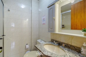 Un baño con lavamanos de mármol, inodoro, ducha y espejo sobre el lavamanos.