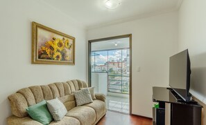 Uma sala de estar com sofá, um quadro, televisão e uma varanda com vista para a cidade.