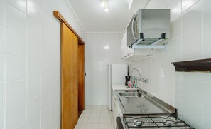 Cozinha compacta com azulejos brancos, fogão a gás, micro-ondas e porta de madeira.