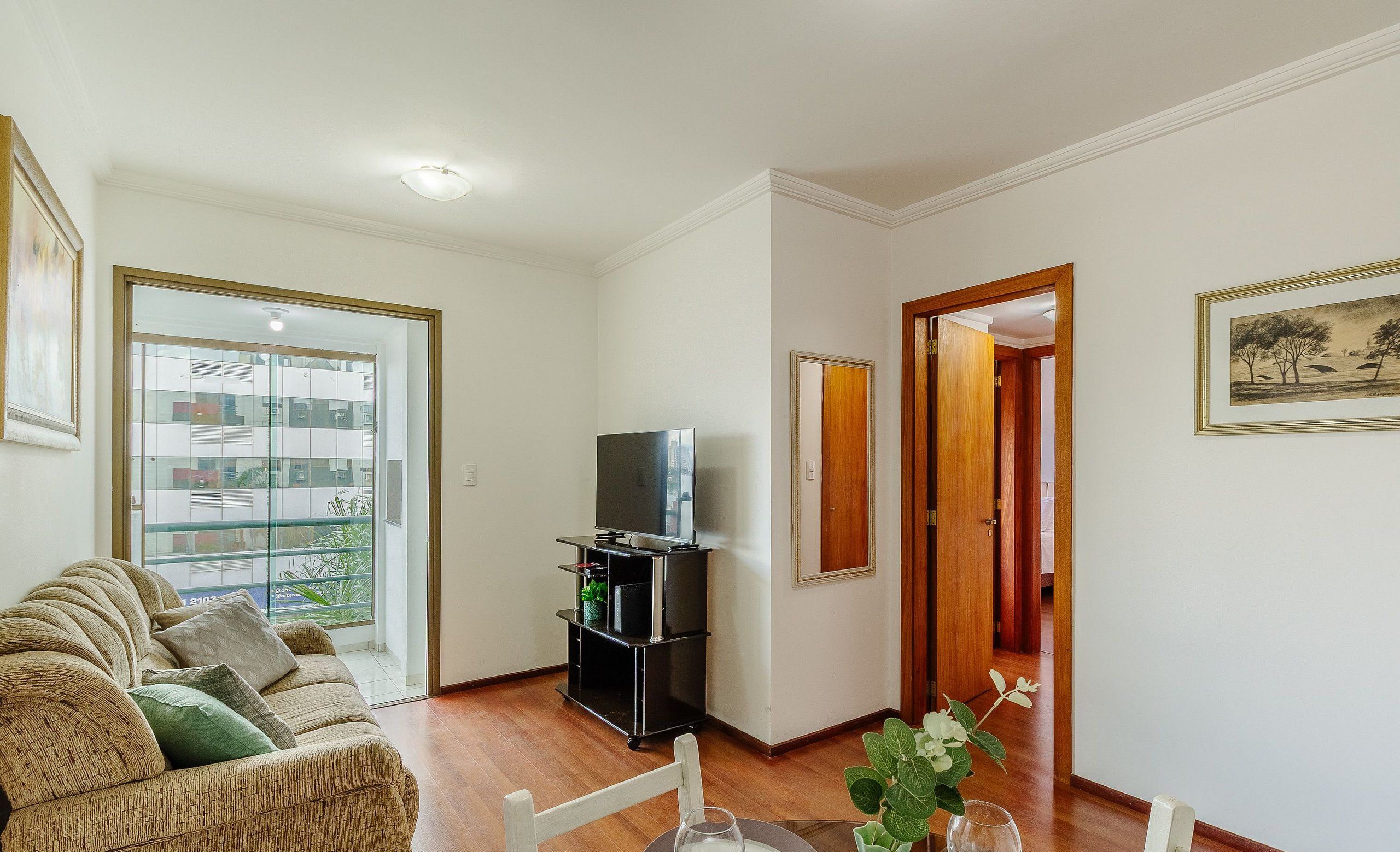 Un soggiorno con divano, televisore su mobile, tavolo da pranzo con sedie e vista su un balcone esterno attraverso una porta vetrata.