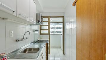 Una cocina estrecha con armarios blancos, un lavamanos de acero inoxidable y una puerta de madera que da a un balcón.