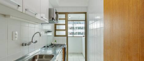 A narrow kitchen with white cabinets, a stainless steel sink, and a wooden door leading to a balcony.