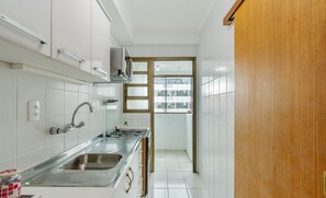 Eine schmale Küche mit weißen Schränken, einer Edelstahlspüle und einer Holztür, die auf einen Balkon führt.