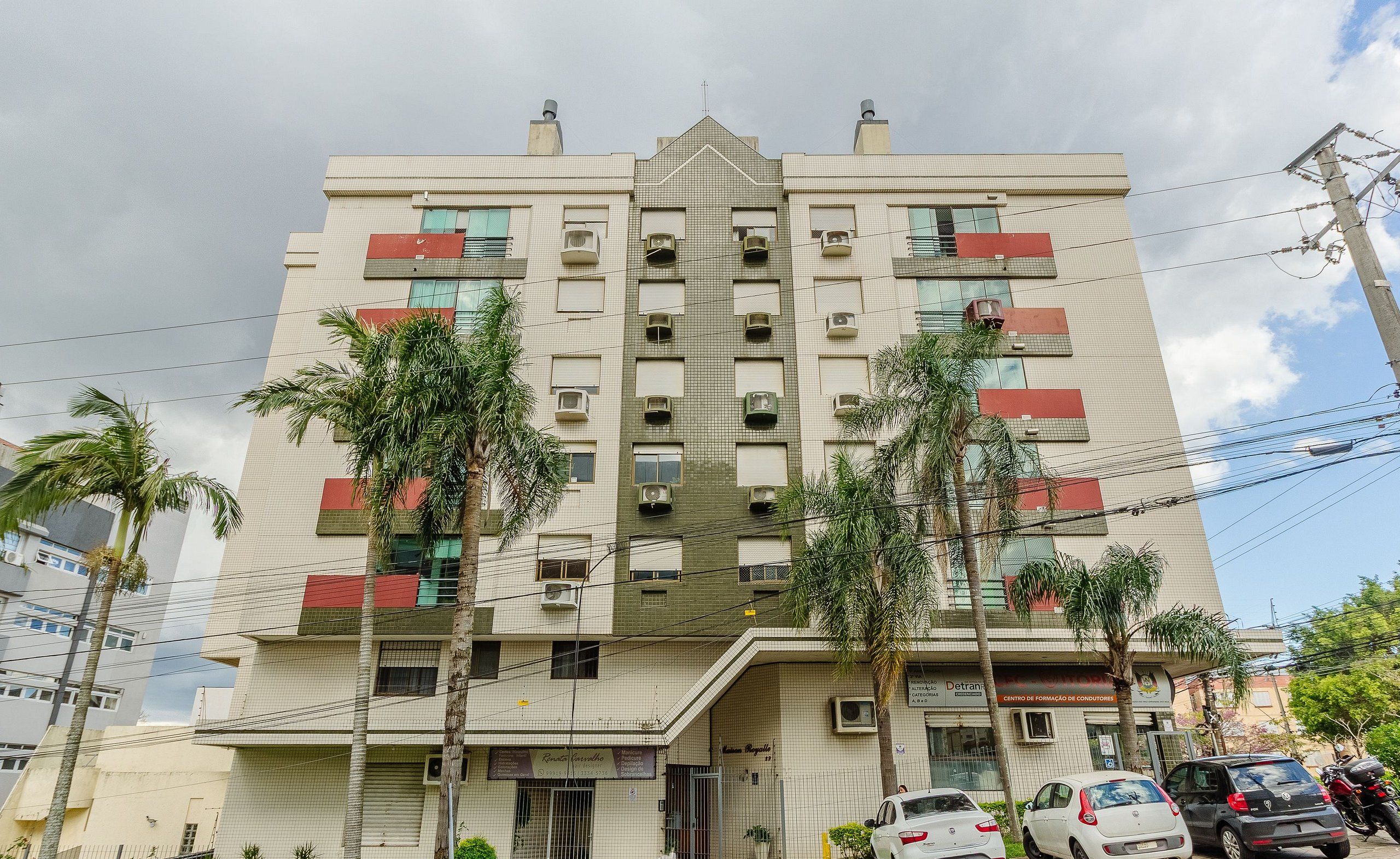 Un edificio de varios pisos con entrada central, unidades de aire acondicionado y un letrero que indica un espacio comercial.