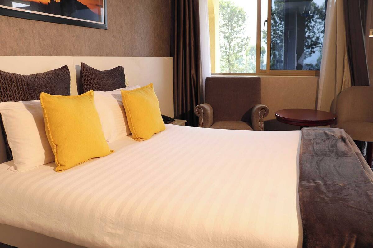 A hotel room with a large bed, two armchairs, a small table, and a window with curtains.