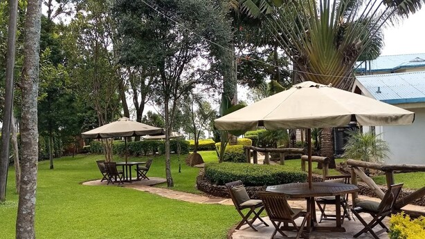 A well-maintained outdoor patio area with round tables and chairs, surrounded by lush greenery and palm trees. - The Exotic House Kericho (Kericho)