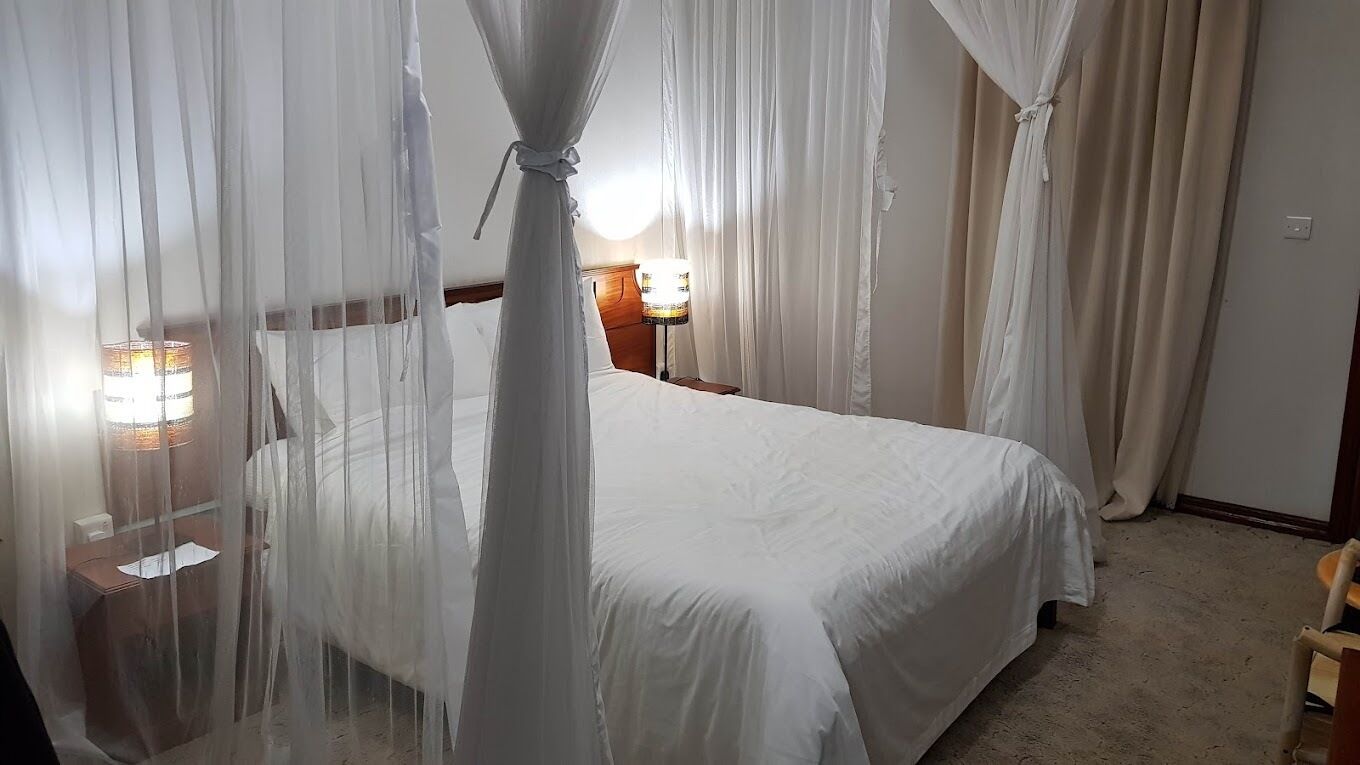A bedroom with a bed covered by a canopy, a bedside table with a lamp, and a nightstand with a lamp.
