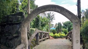 A stone pathway leading through a rustic wooden archway surrounded by lush greenery and a stone wall. - The Exotic House Kericho (Kericho)