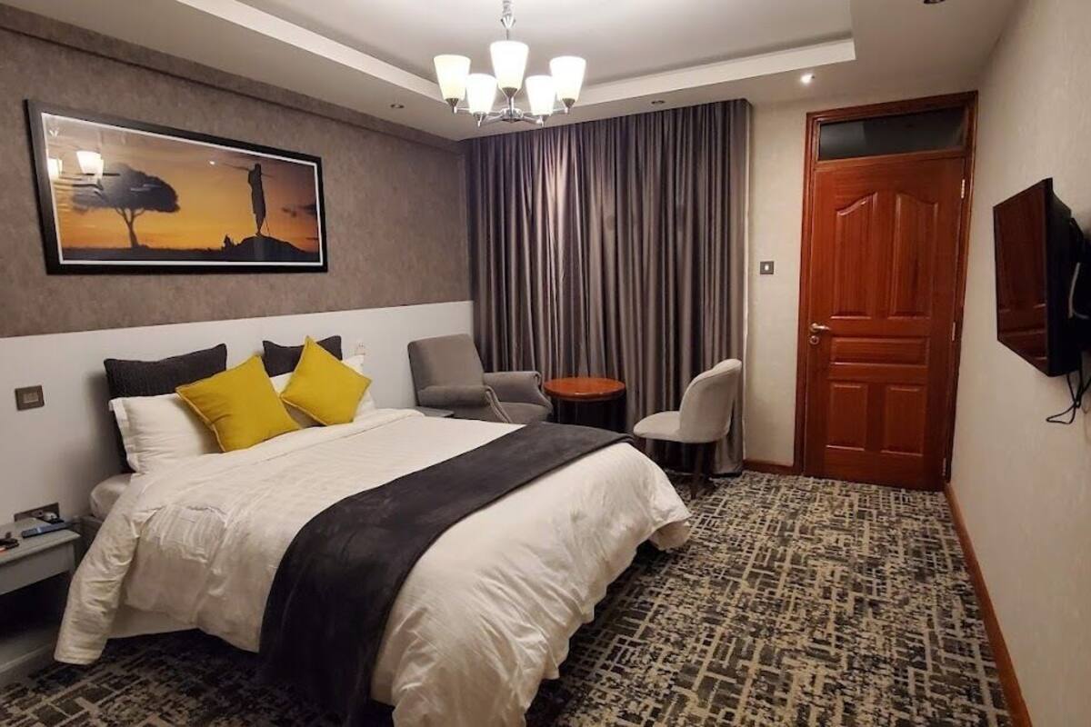 A hotel room with a bed, a desk, a chair, a television, and a door.