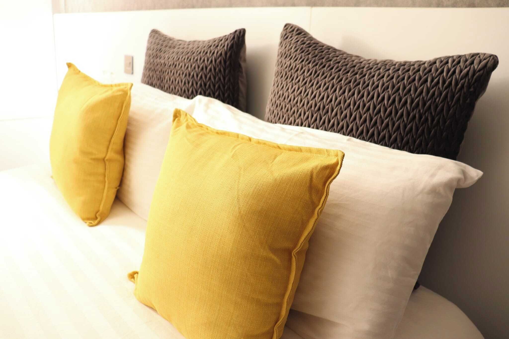 Ein Bett mit drei Kissen in Gelb und Grau.