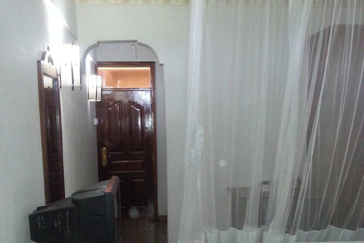 A bedroom with a bed, a television on a table, and a door leading to another room.