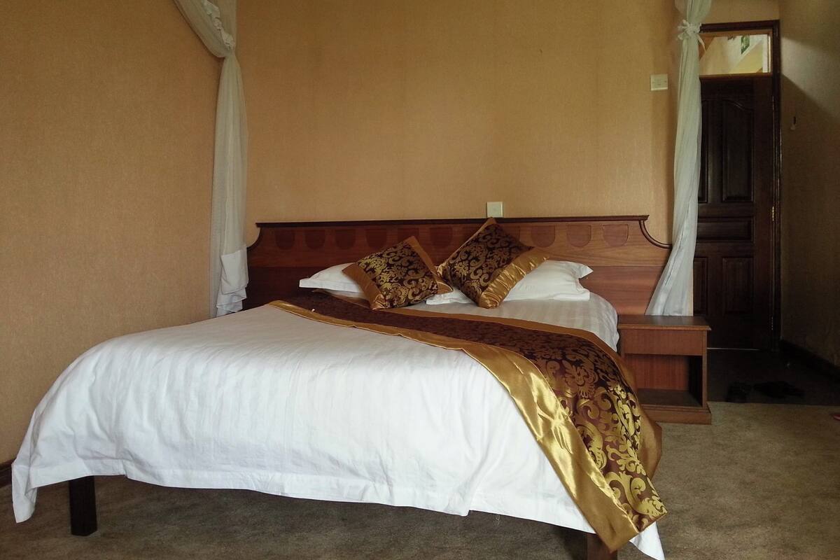 A neatly made bed with a white and gold bedspread, two decorative pillows, and a wooden headboard.