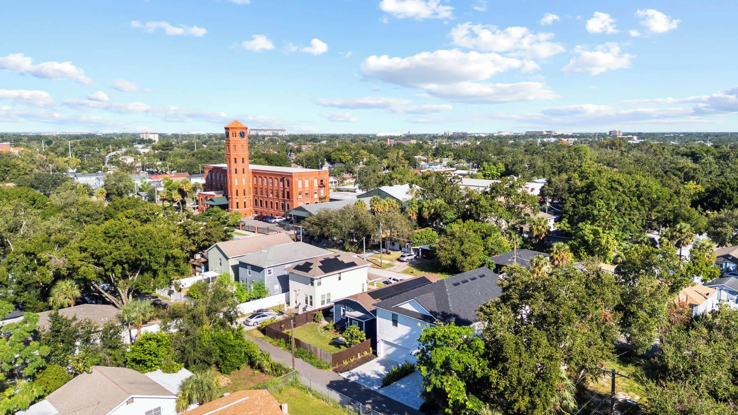 A residential area with a prominent red brick building featuring a clock tower, surrounded by lush greenery and houses.