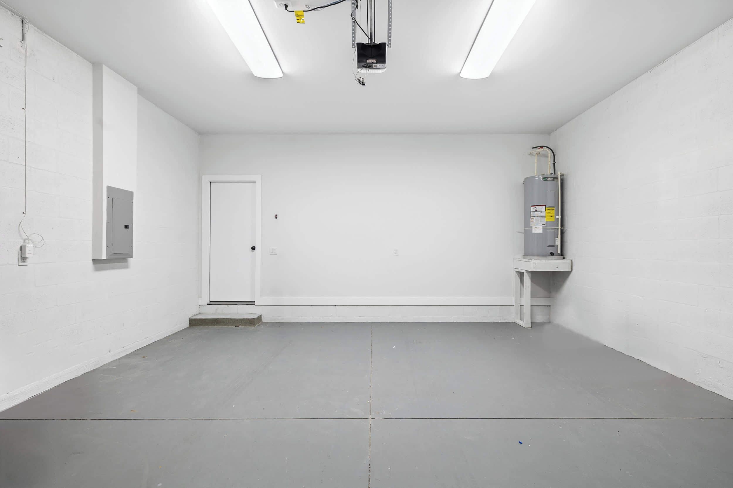 Een schone, lege kamer met witte wanden en een grijze vloer, met een deur, een geïnstalleerd projectiescherm en een boiler op een voetstuk.