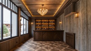 A bar area with a wooden bar counter, shelves of bottles, and a geometric patterned floor. - L'Écrin  (Megève)